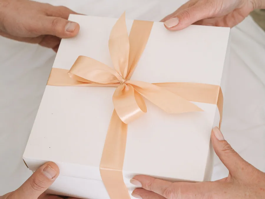 Hands passing a white gift box tied with ribbon